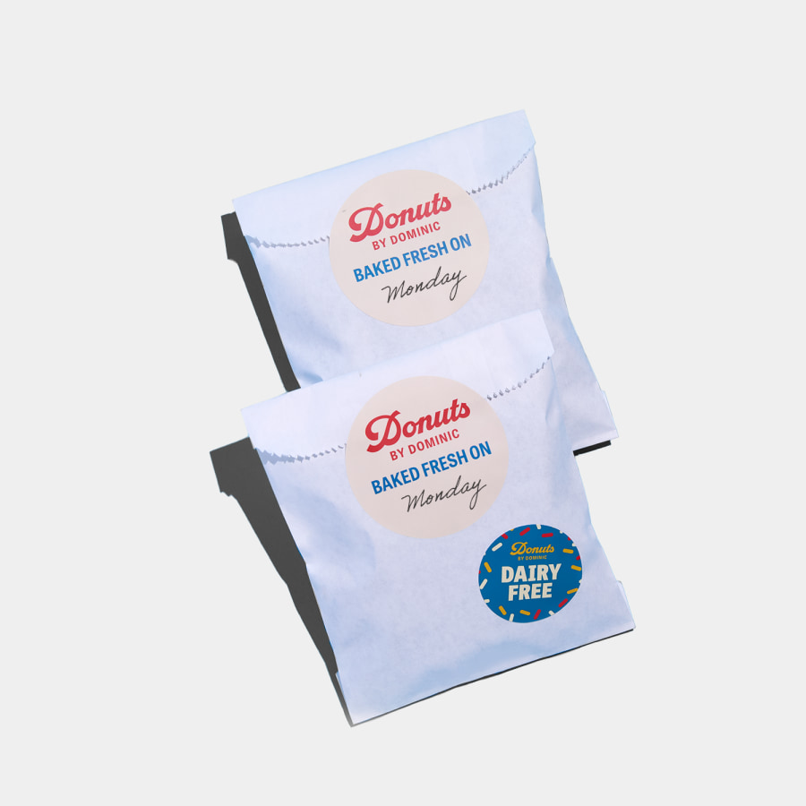 Circle stickers promoting a donut shop, used to seal and label takeaway packaging. 