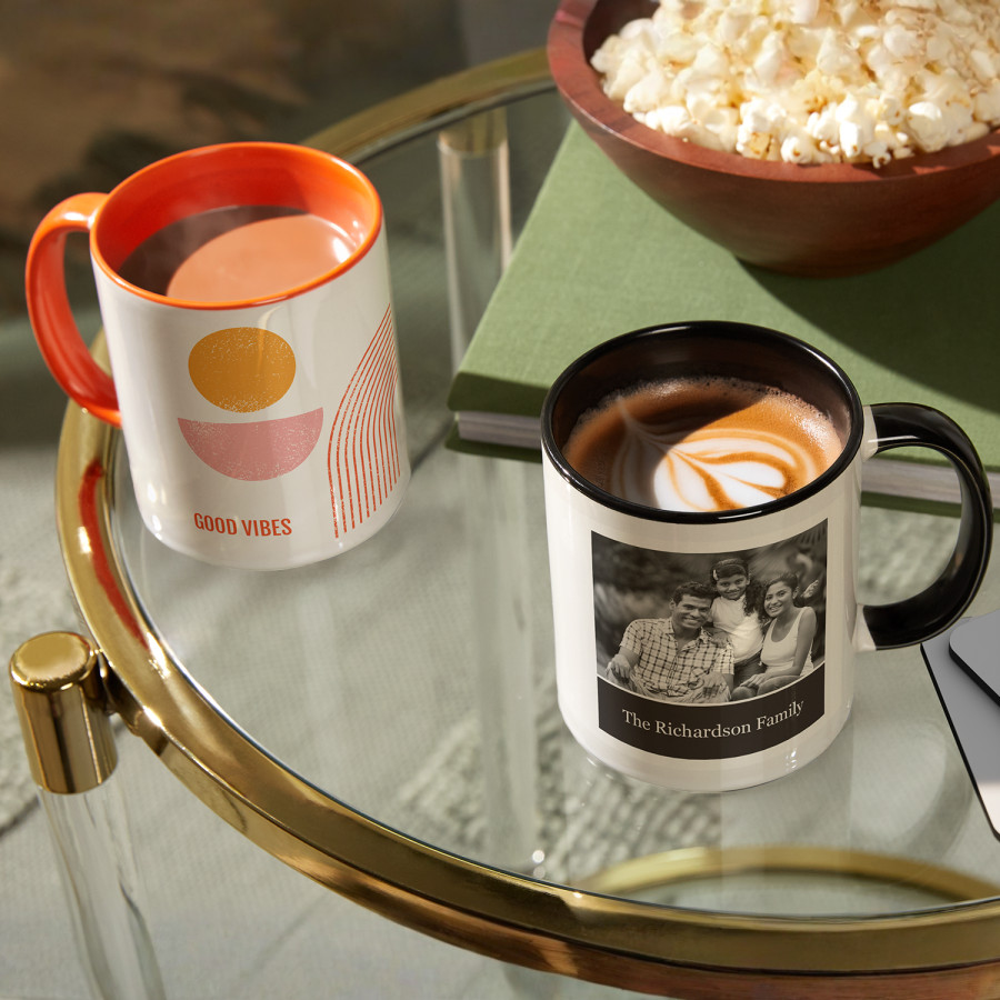 Two mugs on a coffee table, one orange and white, and the other black and white.