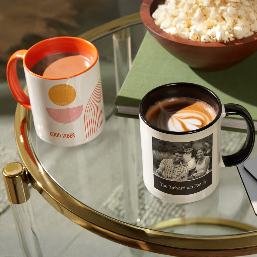 Two mugs on a coffee table, one orange and white, and the other black and white.