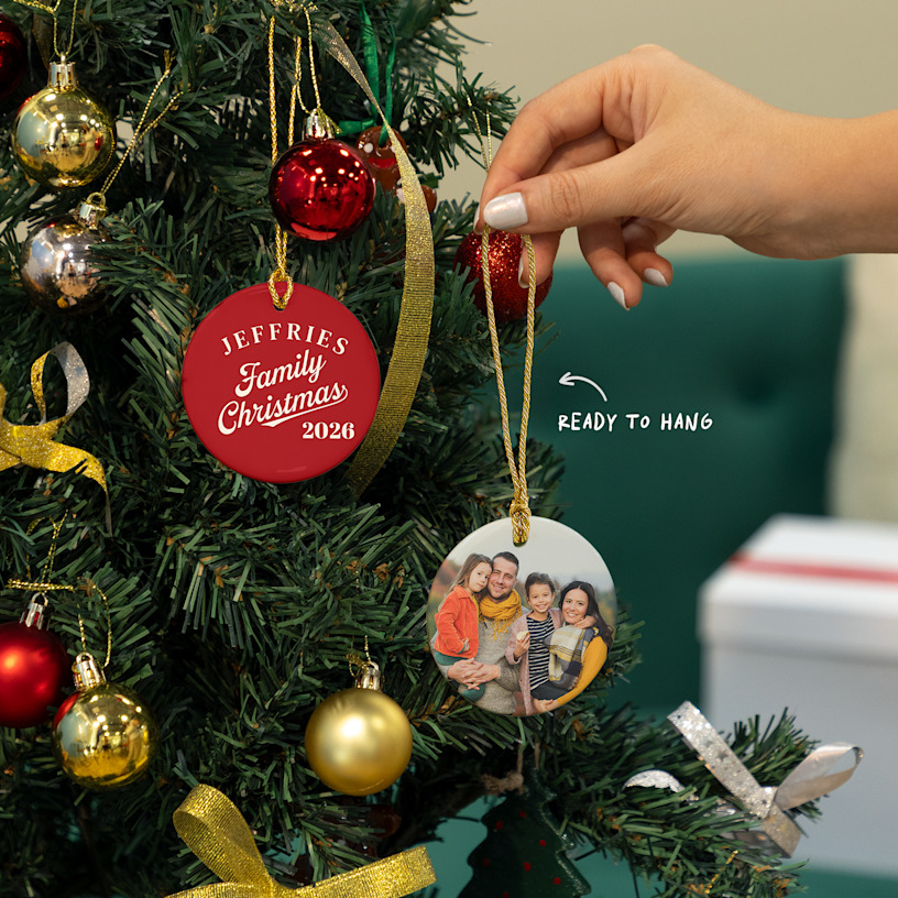 Two Christmas ornaments featuring a family photo and family name, hanging from a tree. An arrow points to the included golden string, which makes the ornaments ready to hang when they arrive.