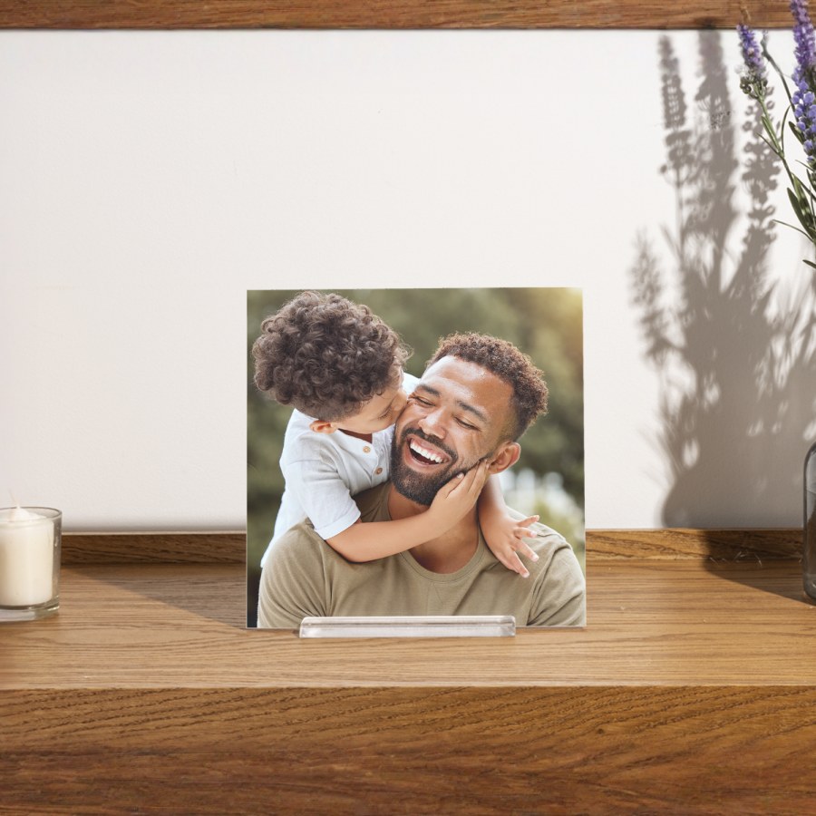 A photo tile printed with a picture of a dad and his son, displayed on a wood tabletop.