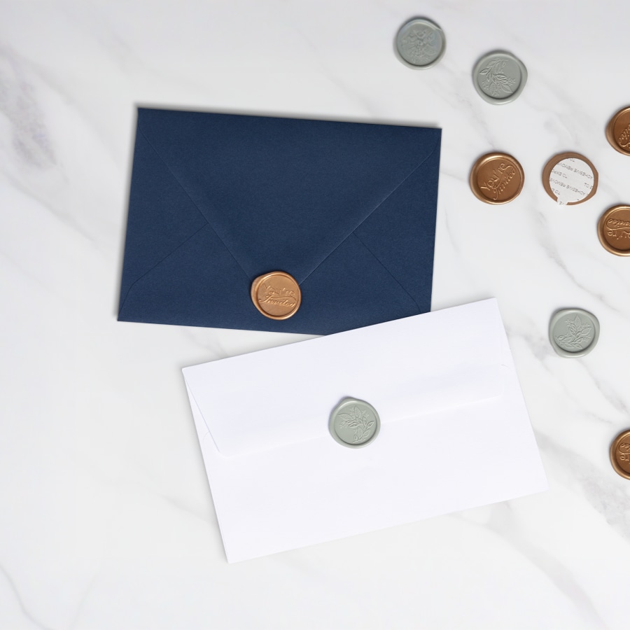 Two envelopes topped with gold-colored wax seals resting on a marble tabletop.