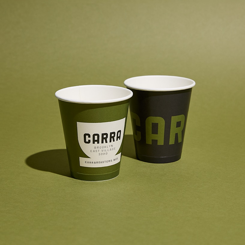 2 customized disposable paper cups on a table next to a paper bag.