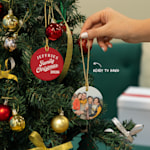 Two Christmas ornaments featuring a family photo and family name, hanging from a tree. An arrow points to the included golden string, which makes the ornaments ready to hang when they arrive.