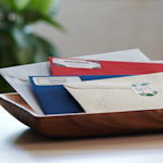 A small pile of colored envelopes in a variety of hues, stacked on a wooden tray. 