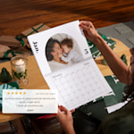A woman holding a photo wall calendar open to a picture of her and her infant son. 