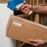 A person using a labeling machine to apply return address labels to a package.