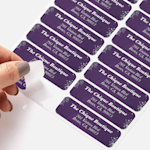 A person peeling a return address label for a boutique from a sheet of labels.