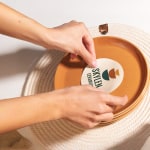 A person applying a packaging label from a ceramics company to a plate.