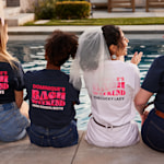 A small group of women sitting by a pool and wearing bachelorette trip shirts.    