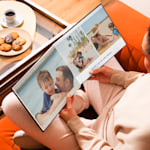 A pair of hands holding an open photo book over a coffee table. The photos show a family at the beach.