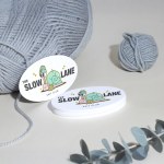 A stack of oval business cards for a knitting club, with yarn and plants in the background.