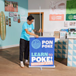 A man setting up his poke bowl retractable banner in a vibrant restaurant setting.