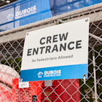 A construction company yard sign with grommets hung up on a fence.