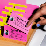 Pink and yellow business cards for a vintage shop in a wooden holder, with a hand pulling one out.