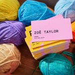 A stack of business cards placed on colorful yarn balls, with the top card showing the backside design.