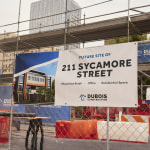  A vinyl banner with grommets hanging on a fence promoting a new mixed use retail building.