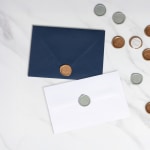 Two envelopes topped with gold-colored wax seals resting on a marble tabletop.
