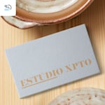 A light gray, textured business card for a ceramics studio on a wooden surface near a ceramic cup, with a 48-hour delivery icon in the corner.