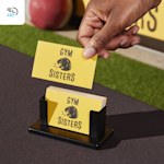 A person picking up a yellow business card for a gym from a small black stand on an outdoor table, with a 48-hour delivery icon in the corner.