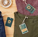 Plastic hang tags pinned into shirts and jeans on a wooden countertop.