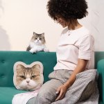A woman sitting on a couch with her cat while she looks at cat face pillow featuring her furry friend printed on it.