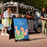Un panneau SignicadeMD noir orné d’une tulipe devant un camion vendant toutes sortes de fleurs.