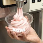 A plastic ice cream cup with a few scoops of ice cream, nuts and a waffle topping.