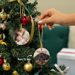 A Christmas ornament featuring a photo of two children, along with a festive greeting. An arrow points to the pre-drilled hole and gold string.