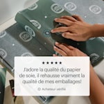 Deux mains en train d’envelopper une boîte cadeau de papier de soie avec impression personnalisée, et un avis client disant :
« J’adore la qualité du papier de soie. Ça améliore vraiment mes emballages! »