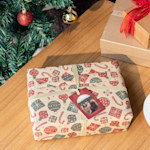A wrapped present topped with a custom ornament and placed alongside a Christmas tree.