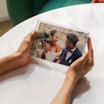 Manos sosteniendo un bloque de acrílico transparente con una foto que muestra el retrato de boda de una pareja recién casada.