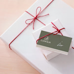 Una targhetta per regalo personalizzata con un design natalizio, infilata sotto il nastro di un regalo incartato. 