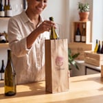 A woman packing a bottle of wine into a brown kraft wine bag.
