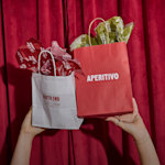 A pair of hands holding up two paper bags filled with tissue paper customized for an Italian restaurant. Highlighted benefits include full-color printing, free design assistance, free shipping and the ability to create your own tissue paper pattern.