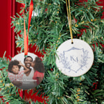 Two custom ornaments hanging from a Christmas tree, one printed with a monogram and the other with a photo of a mother and her two daughters.