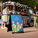 A black Signicade® with a tulip on it in front of a truck selling a variety of flowers.