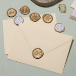 Ein cremefarbener Umschlag mit einem goldenen Wachssiegel sowie weitere selbstklebende Wachssiegel auf einer Oberfläche verstreut.
