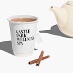A full-print cup filled with tea next to a tea pot and cinnamon sticks.