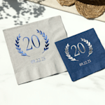 Two foil napkins for a birthday, one featuring blue foil and the other featuring silver foil.