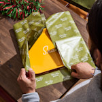 A woman wrapping a yellow gift box in tissue paper customized for an Italian restaurant.