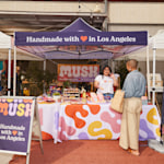 A handmade goods store set up underneath a canopy tent in an outdoor market.