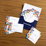 A spread of colorful, rounded-corner business cards arranged on a wooden surface with an open card holder displaying multiple cards.
