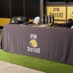 tradeshow rectangle table with branded tablecloth displaying branded apparel and promotional products for a gym business