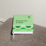 A hardcover diary on top of a sofa’s armrest promoting a design company.
