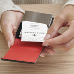 A woman is removing a card from a black leather vertical business card holder.