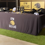 tradeshow rectangle table with branded tablecloth displaying branded apparel and promotional products for a gym business