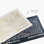 Two standard business cards with different metallic foil designs for the same person, with a note highlighting the gold and silver foil options.