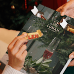 "Person taking out a small Toblerone chocolate from a custom advent calendar featuring the logo of a home decor business Lumah.  "