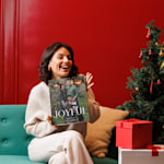 A smiling woman sat next to a Christmas tree, holding a personalised photo advent calendar.